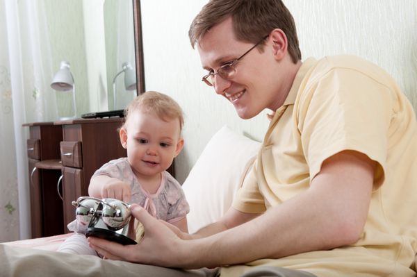 پدر جوان در حال نشان دادن ساعت زنگ دار به دختر کوچکش