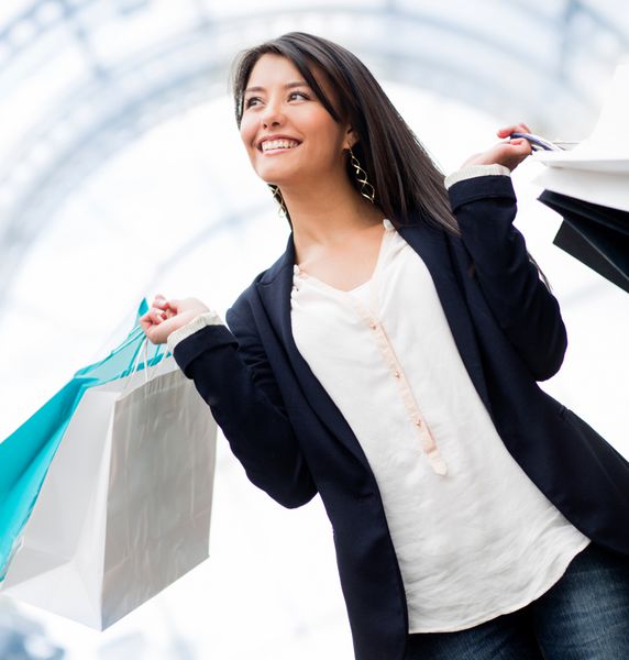 زن شادی که در مرکز خرید خرید می کند و کیف در دست دارد