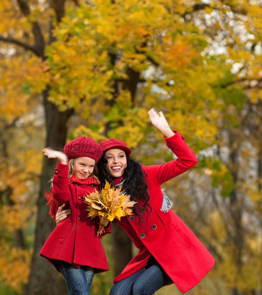 زن و دختر جوان قفقازی جذاب با لباس های رنگارنگ گرم با برگ های زرد در فضای باز و خندان