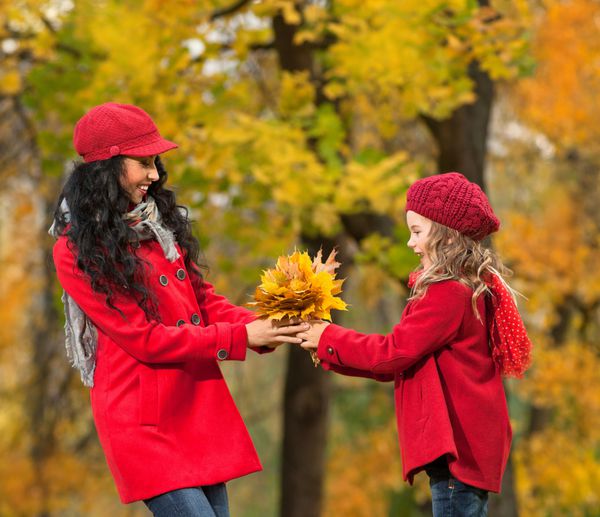 زن و دختر جوان قفقازی جذاب با لباس های رنگارنگ گرم با برگ های زرد در فضای باز و خندان
