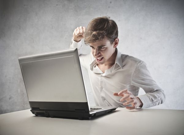 تاجر جوان خشمگین در حال مشت زدن به لپ تاپ خود است
