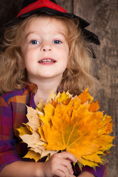 بچه شادی که برگ های پاییزی را در دست دارد مفهوم هالووین