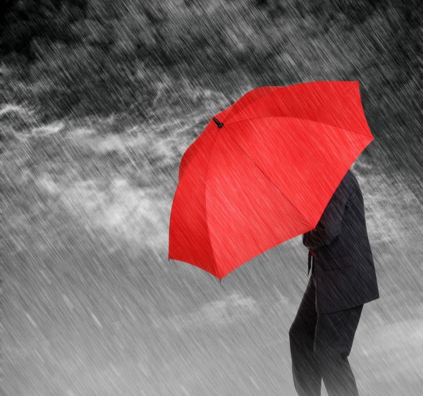 تاجر با چتر قرمز از خود در برابر مفهوم طوفان برای محافظت در برابر رکود یا رکود اقتصادی و غیره محافظت می کند