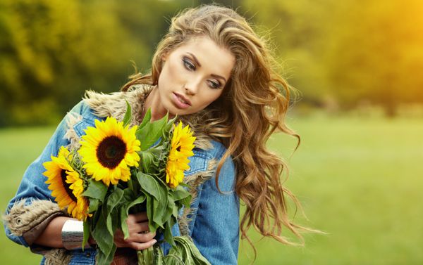 زن جوان مد با یک دسته گل آفتابگردان در مزرعه