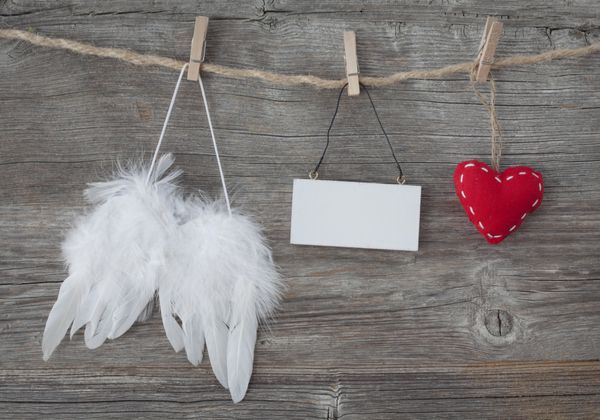 بال های فرشته با قلب و یادداشت خالی در زمینه چوبی خاکستری