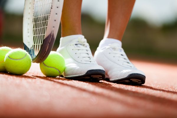 پاهای ورزشکار در نزدیکی راکت تنیس و توپ