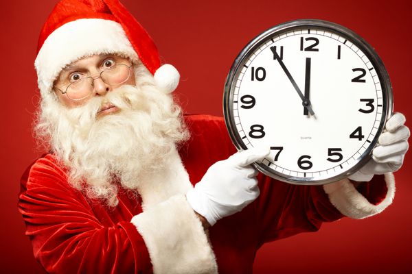 عکس بابا نوئل حیرت‌زده که ساعتی را در دست دارد که پنج دقیقه مانده به نیمه‌شب را نشان می‌دهد