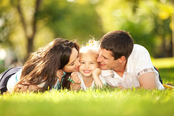 مادر و پدر خوشحال در حال بوسیدن دخترشان در پارک
