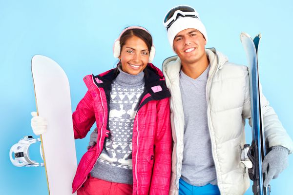 پرتره دختر زیبا و مرد خوش تیپ با لباس زمستانی که اسنوبرد و اسکی در دست دارد