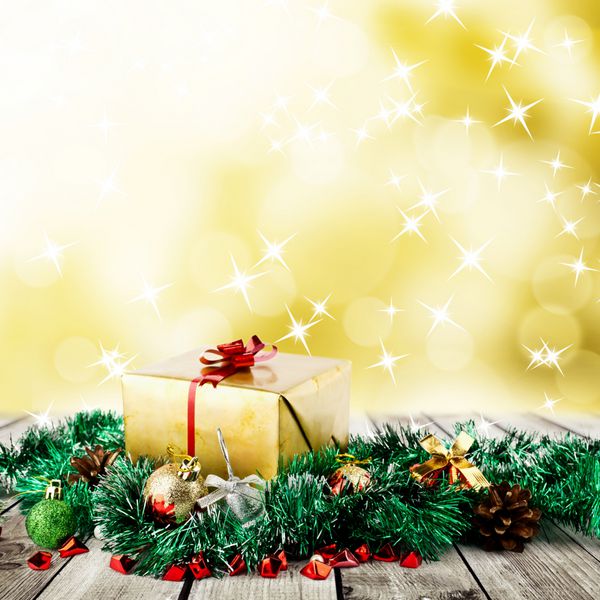 جعبه هدیه کریسمس طلایی با توپ های کریسمس روی تخته های چوبی روی پس زمینه زرد تار انتزاعی