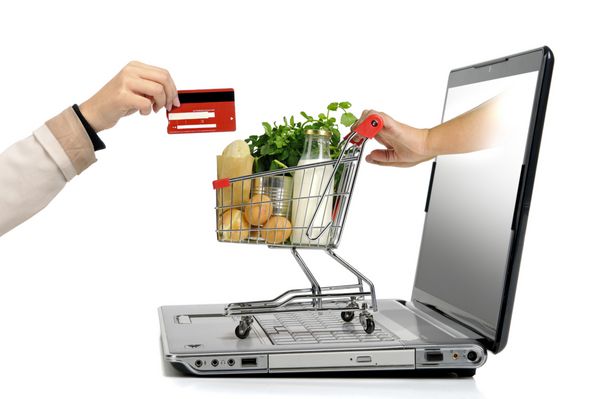 دستی با کارت اعتباری و یک سبد خرید کوچک که از صفحه نمایش لپ تاپ به رنگ سفید جدا شده است