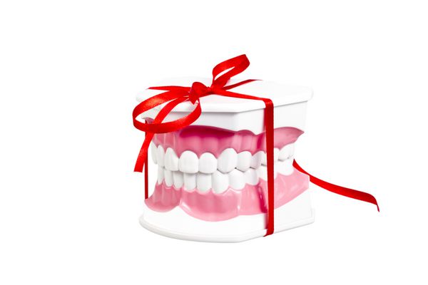 فک انسان مصنوعی با دندان های سفید که به عنوان هدیه با روبان قرمز نشان داده شده است