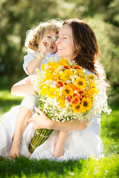 کودک و زن شاد با دسته گل های بهاری که روی چمن سبز نشسته اند مفهوم روز مادر
