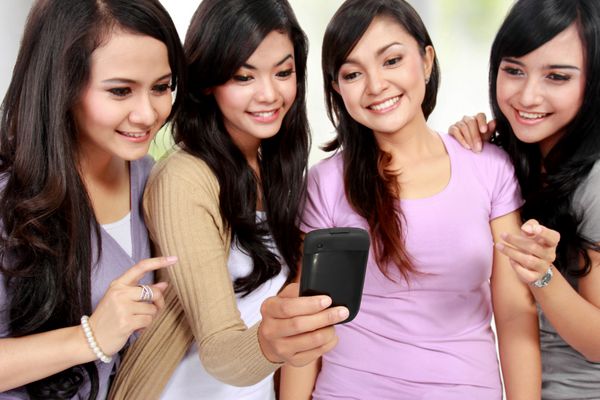 چهار دوست زن جوان زیبا در خانه با هم از تلفن همراه استفاده می کنند
