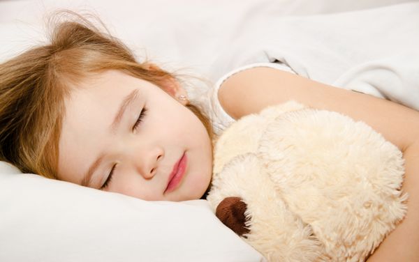 دختر کوچولوی دوست داشتنی که با اسباب بازی خود روی تخت خوابیده است