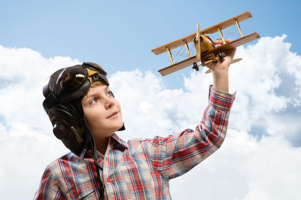 پسر خلبان کلاه ایمنی در حال بازی با یک هواپیمای چوبی اسباب بازی در ابرها در آرزوی خلبان شدن