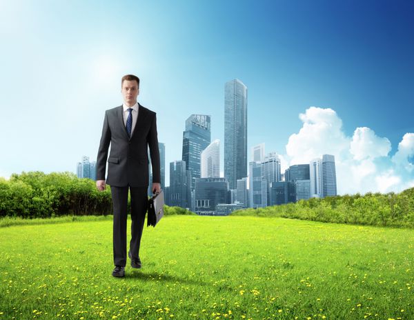 مرد تجاری در حال قدم زدن در زمین سبز و شهر مدرن