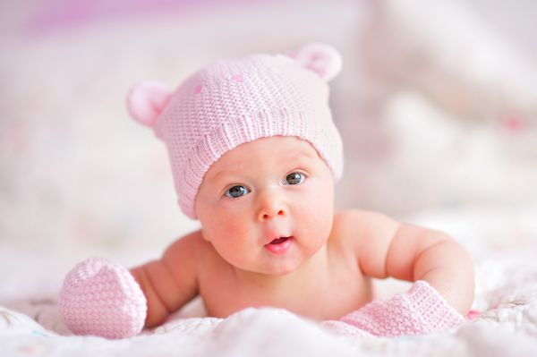 دختر نوزاد تازه متولد شده با کلاه خرس بافتنی صورتی و دستکش روی تخت