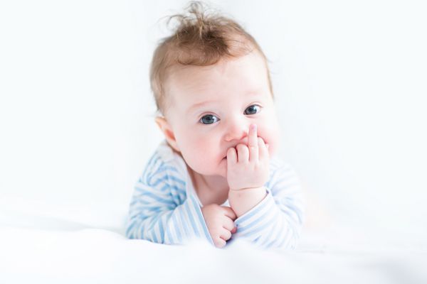 کودک شیرین با پیراهن آبی در حال مکیدن انگشتش