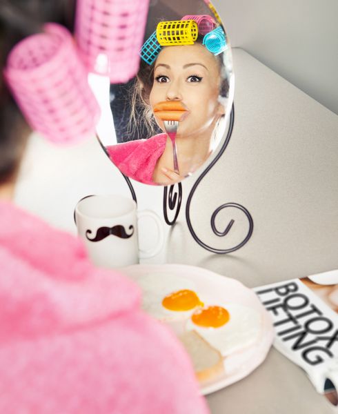 زنی با سوسیس روی چنگال در حال شبیه‌سازی لب‌ها هنگام صرف صبحانه