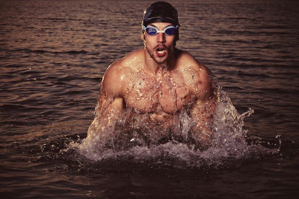 شناگر عضلانی خوشحال با عینک و کلاه در استخر شنا و مفهوم سلامت و تناسب اندام را نشان می دهد