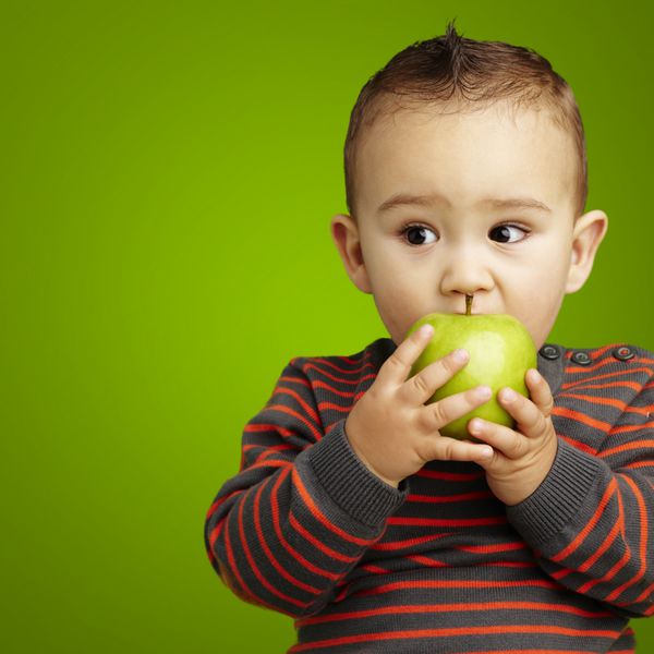 پرتره یک بچه خوش تیپ که یک سیب سبز را روی پس زمینه سبز گاز می گیرد