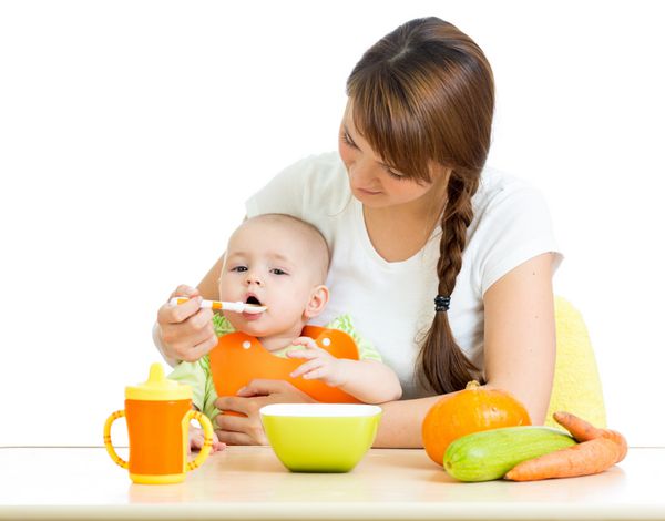 قاشق مادر جوانی که به نوزادش جدا شده روی سفید غذا می دهد