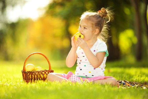 دختر بچه ناز در حال خوردن سیب در پارک