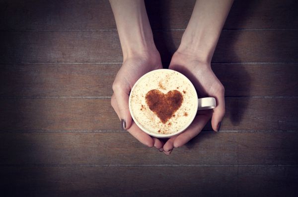 زنی که فنجان قهوه داغ با شکل قلب در دست دارد