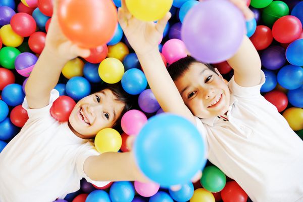 کودکان شاد در حال بازی و سرگرمی در مهد کودک با توپ های رنگارنگ