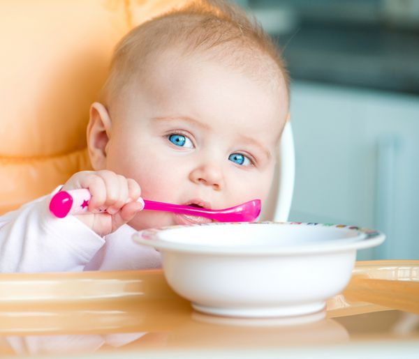 دختر بچه خندان قاشقی را در دهانش گرفته و می رود غذا بخورد