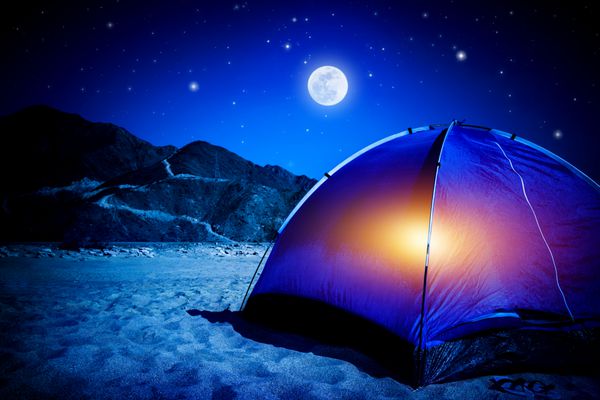 کمپ در ساحل شنی چادر در شب با نور داخل نور ماه گردشگری فعال پیاده روی و مفهوم مسافرت