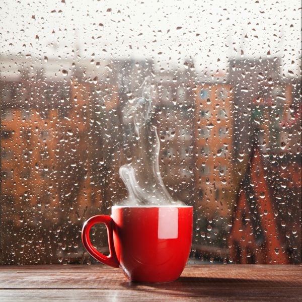 فنجان قهوه بخارپز در پس زمینه پنجره روز بارانی