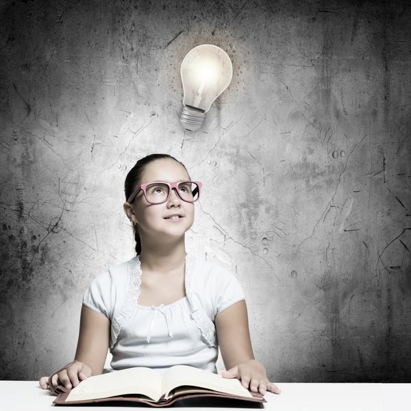 دختر زیبای مدرسه با عینک قرمز در حال خواندن کتاب