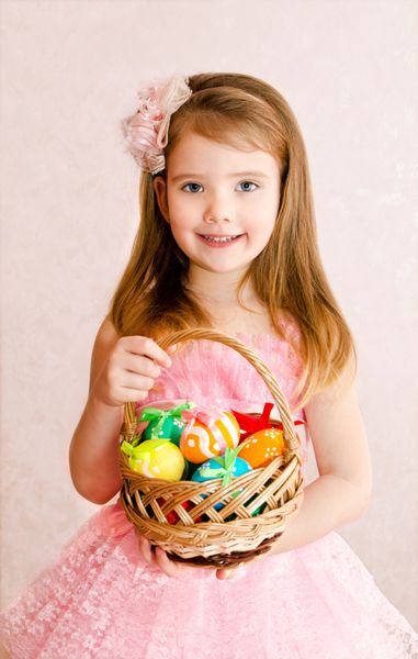 دختر کوچک خندان با سبدی پر از تخم مرغ های رنگارنگ عید پاک