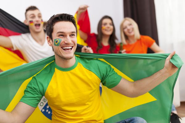 مرد برزیلی با دوستانی از کشورهای مختلف در حال لذت بردن از فوتبال در تلویزیون