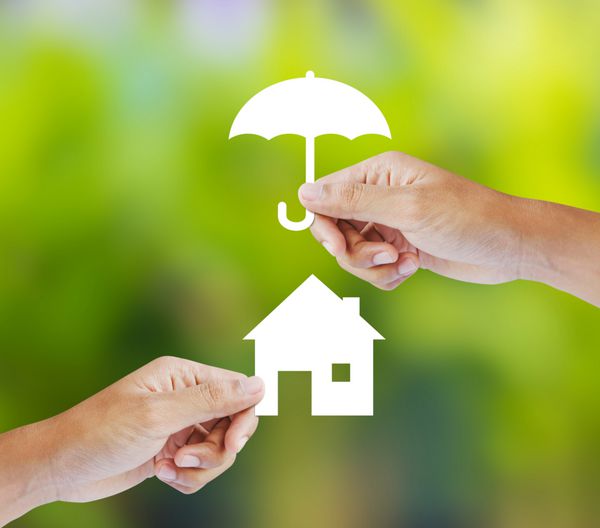 دستی که خانه کاغذی و چتر در پس زمینه سبز در دست گرفته است
