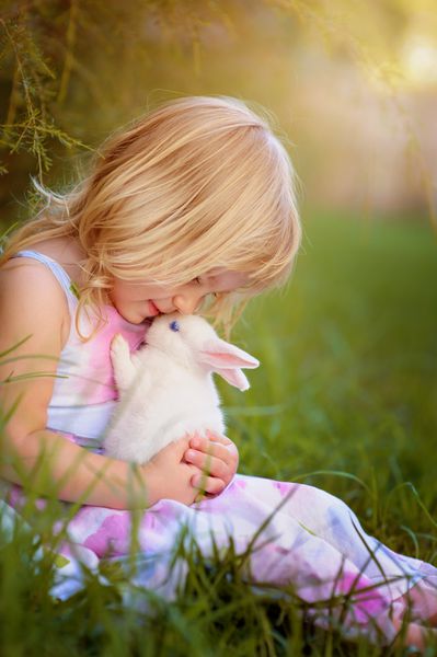 دختر کوچولوی ناز با خرگوش خرگوش عید پاک در پس زمینه چمن سبز دارد