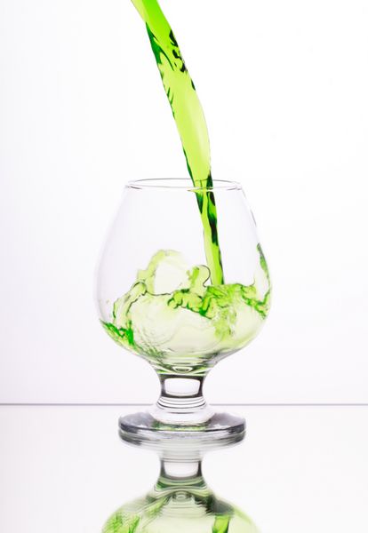 کوکتل الکل سبز در شیشه با چلپ چلوپ در پس زمینه سفید تمرکز انتخابی بر روی جت مایع