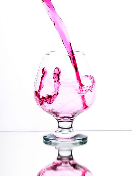 کوکتل الکل صورتی در شیشه با چلپ چلوپ در پس زمینه سفید تمرکز انتخابی بر روی جت مایع