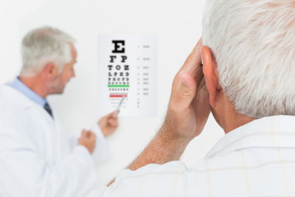 چشم پزشک اطفال مرد با بیمار ارشد که به نمودار چشم در مطب اشاره می کند