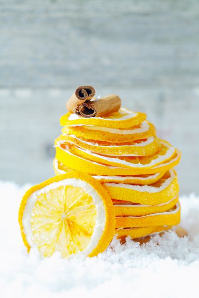پشته ای از تکه های پرتقال خشک و دارچین روی برف برای چاشنی نوشیدنی های گرم و دسر در زمستان سرد