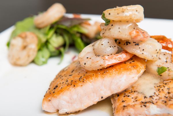 ماهی قزل آلا کبابی با سس سفید خامه ای که با سبزیجات بهاری و میگو سرو می شود