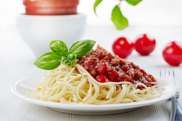 اسپاگتی بولونیز و برگ ریحان سبز در بشقاب سفید