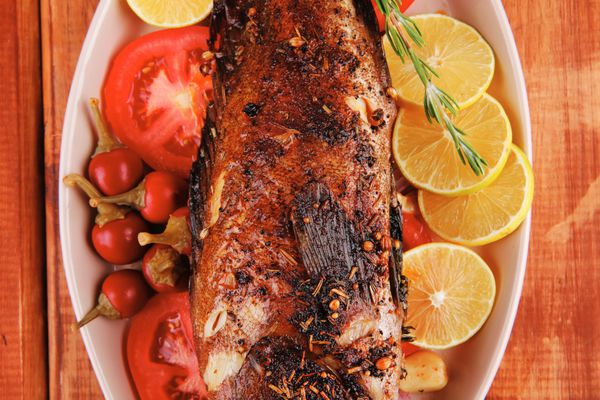 ناهار سالم آفتاب ماهی دریایی سرخ شده کامل روی میز چوبی با فلفل لیمو و گوجه فرنگی و شاخه رزماری