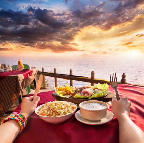 سوپ گیاهی هندی سوپ ذرت و برنج سرخ شده روی میز در اقیانوس و پس‌زمینه غروب شگفت‌انگیز دست با چنگال و چاقو روی میز