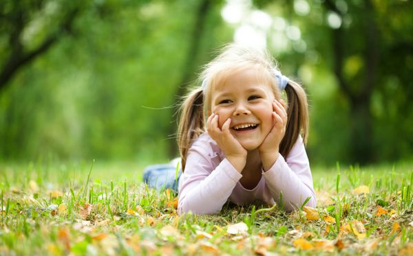 دختر کوچولوی ناز در پارک پاییز با برگ ها بازی می کند
