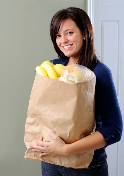 زن جوان زیبا در حال بازگشت به خانه با یک کیسه مواد غذایی