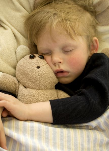 کودک خوابیده زیبا که خرس عروسکی را در آغوش می گیرد