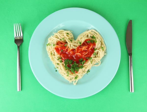 اسپاگتی پخته شده با دقت به شکل قلب چیده شده و با سس گوجه فرنگی روی زمینه رنگی ریخته شده است